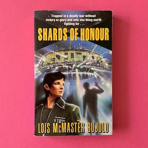 May include: A paperback book titled Shards of Honour by Lois McMaster Bujold. The cover features a person in a dark green uniform, a silhouette of a person, and a large spacecraft with bright lights. Text reads: Trapped in a deadly war without victory or glory and only one thing worth fighting for.