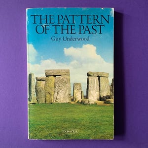 以下が含まれることがあります： ガイ・アンダーウッド著『The Pattern of the Past』のペーパーバック。表紙には、緑の芝生の上に広がる明るい青空と白い雲を背景に、大きな灰色の石の巨石群が写るストーンヘンジの写真が掲載されています。アバカス社のロゴ入り。