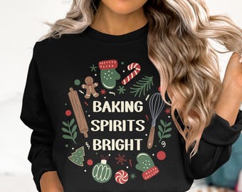 May include: Black sweatshirt with a festive design. The design includes a gingerbread man, rolling pin, whisk, candy cane, and the text "BAKING SPIRITS BRIGHT" in white. Christmas-themed apparel.
