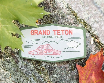 May include: A green and white embroidered patch with the text "Grand Teton National Park" and a red cabin illustration.