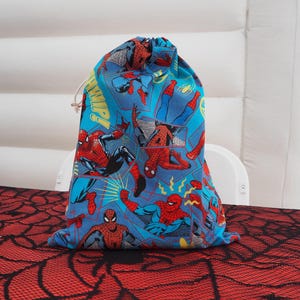 May include: A blue drawstring bag with a Spiderman theme. The bag features multiple images of Spiderman in various poses, with a blue background and yellow accents.