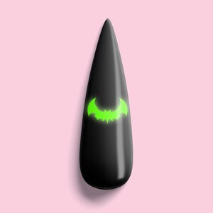 May include: Black nail with a green bat design. The nail is on a pink background. The text "SIMPLYCRYSTAL nails" is below the nail.