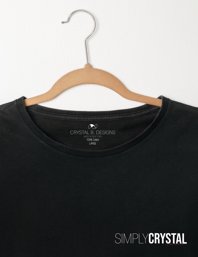 以下が含まれることがあります： 白いタグに「Crystal B. Designs Made in New York 100% Cotton Large」と書いてある黒いTシャツ。Tシャツの下部に「Simply Crystal」の文字が印刷されています。