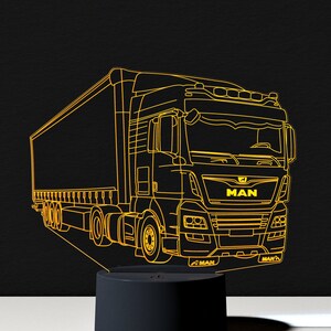 Op de afbeelding: Een gele omtrek van een vrachtwagen met het woord "MAN" aan de voorkant. De vrachtwagen staat op een zwarte basis met een wit oppervlak eronder.