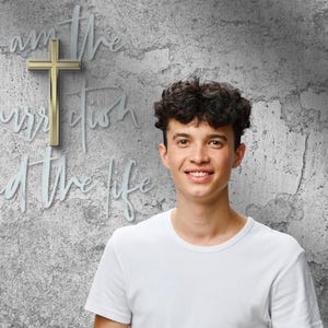 Könnte beinhalten: Eine junge Person in einem weißen T-Shirt lächelt vor einer strukturierten grauen Wand. Ein goldenes Kreuz und die Worte "Ich bin die Auferstehung und das Leben" sind an der Wand zu sehen.