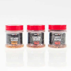 May include: Three small glass jars with red lids containing dried chili peppers. The labels read "Red Savina Habanero", "Carolina Reaper", and "Ghost Pepper".
