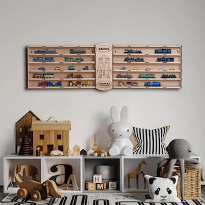 May include: A wooden display shelf with two sections for Thomas & Friends toy trains. The top section is labeled "Daniel" and the bottom section is labeled "Thomas & Friends". The shelf is filled with various toy trains in different colors.