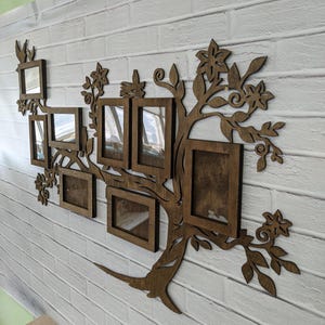 May include: A wooden wall decor in the shape of a tree with multiple photo frames. The frames are arranged in a tree-like pattern with branches and leaves. The frames are all brown and have a rustic look.