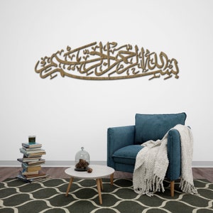 May include: A wooden wall decor with Arabic calligraphy in a living room setting. The decor is mounted on a white wall above a blue armchair and a white coffee table with a glass cloche on top.
