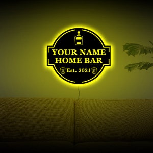 May include: A yellow neon sign with a black background that reads "YOUR NAME HOME BAR Est. 2021". The sign has a bottle and two shot glasses on it.