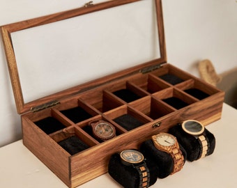 May include: A wooden watch display case with a clear glass lid, showcasing multiple compartments with black velvet inserts. Several wooden watches with various band and face designs are displayed on black velvet pillows.