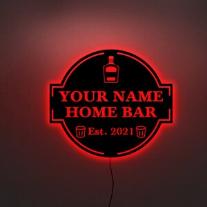 May include: Black and red illuminated sign with the text "YOUR NAME HOME BAR Est. 2021" and a bottle and two shot glasses.
