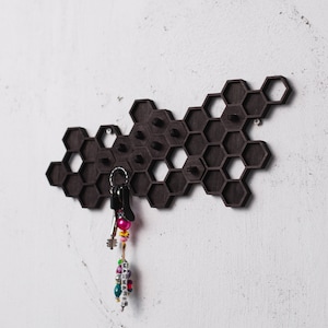 May include: A black honeycomb-shaped key holder with a set of keys and colorful beads hanging from one of the hooks.