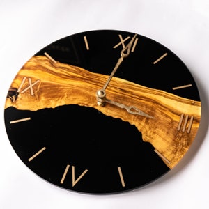 May include: A black and brown clock with Roman numeral markings. The clock face is made of black resin and features a wood grain design. The clock hands are gold.