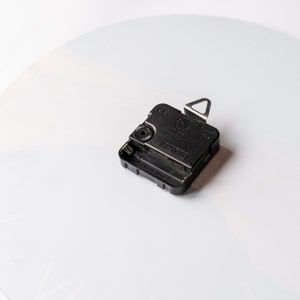 May include: Black clock mechanism with a silver hook on the top. The mechanism has a small knob on the side and the text "Japan Movt" printed on the bottom.