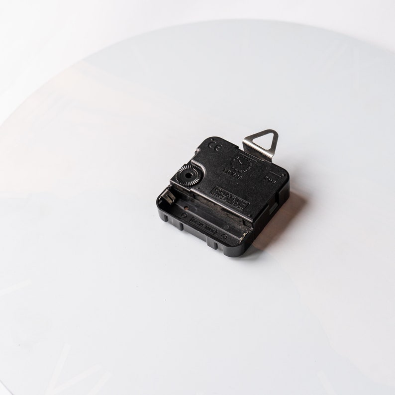 May include: Black clock mechanism with a silver hook on the top. The mechanism has a small knob on the side and the text "Japan Movt" printed on the bottom.