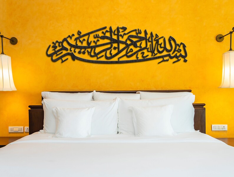 May include: A black wooden wall art piece with Arabic calligraphy on a yellow wall above a white bed with white pillows.