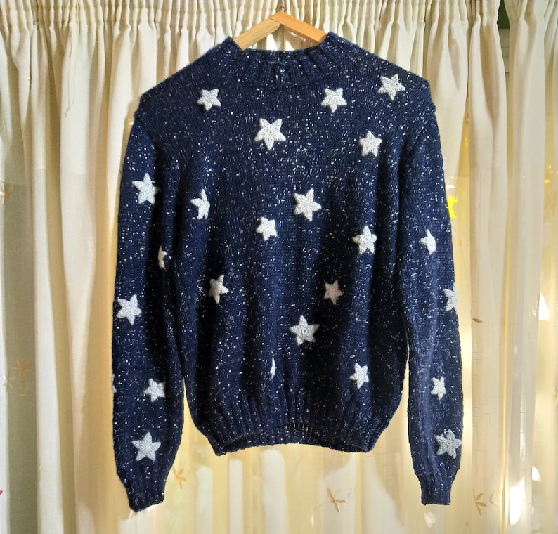 May include: A navy blue sweater with white star-shaped embellishments. The sweater has a sparkly texture.
