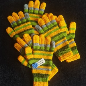 May include: Four pairs of yellow and green striped knitted gloves. The gloves have a grey stripe between each yellow and green stripe. The gloves are arranged in a pile on a black surface. A small blue tag with the text "warm - medium size - crocheted!" is attached to one of the gloves.