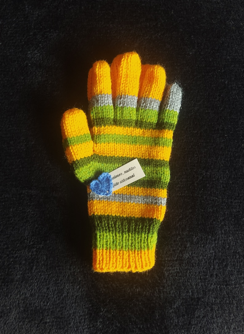 May include: Yellow and green striped knitted gloves with a small blue crocheted flower attached to a tag that reads "creaciones_nuditos tejido artesanal".