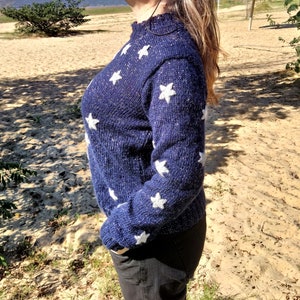 May include: A blue knitted sweater with white star accents. The sweater has a sparkly texture.
