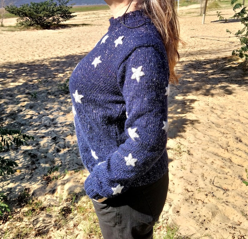 May include: A blue knitted sweater with white star accents. The sweater has a sparkly texture.