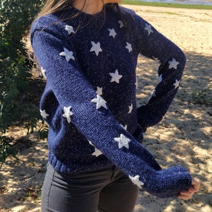 May include: A navy blue sweater with white star-shaped patterns. The sweater is made of a soft, knit fabric.