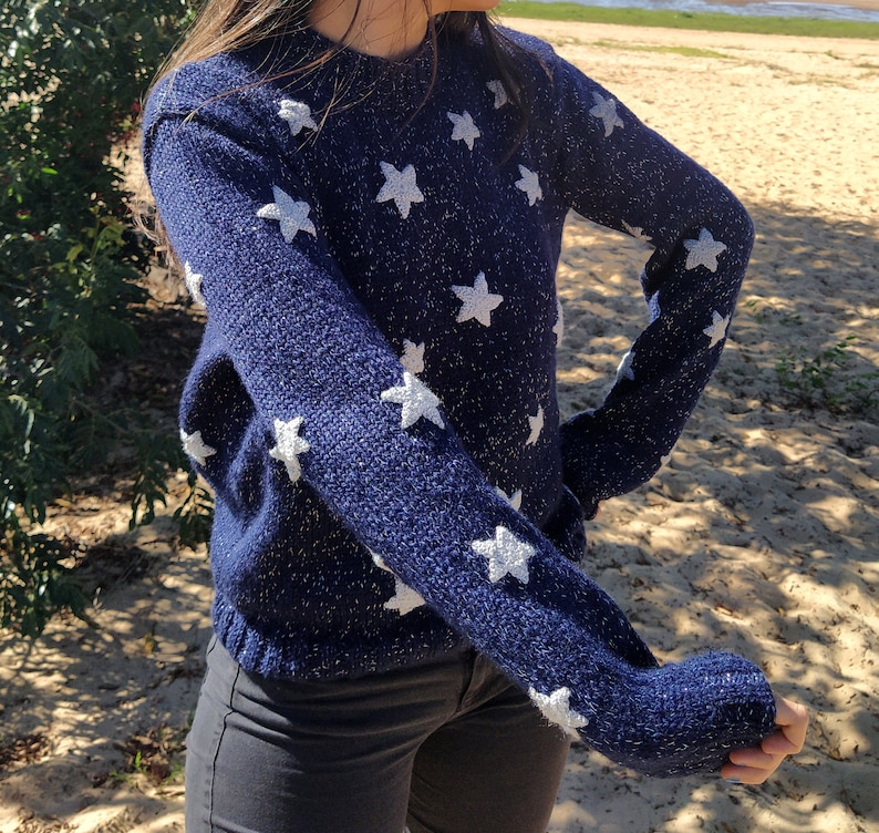 May include: A navy blue sweater with white star-shaped patterns. The sweater is made of a soft, knit fabric.