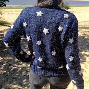 May include: A navy blue sweater with white star-shaped embellishments. The sweater has a sparkly texture.