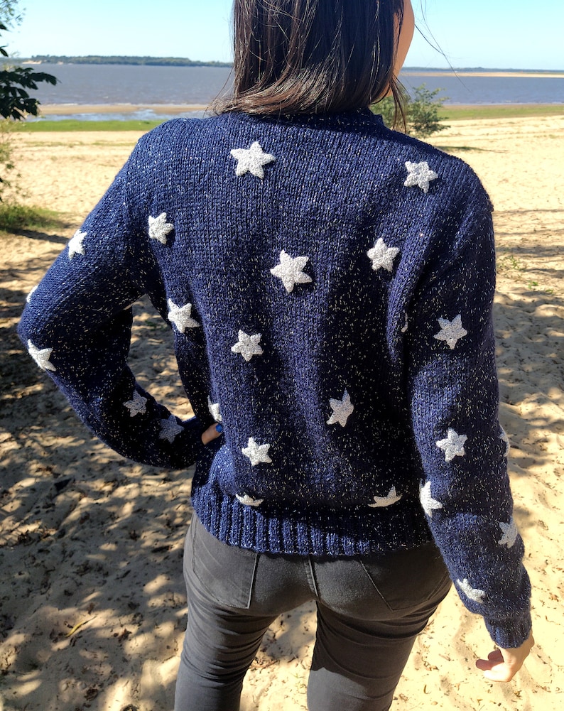 May include: A navy blue sweater with white star-shaped embellishments. The sweater has a sparkly texture.