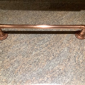 May include: A copper towel bar with two flanges. The bar is mounted on a granite countertop.