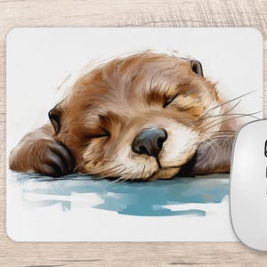 May include: A rectangular mouse mat featuring a watercolour-style illustration of a brown otter sleeping with its eyes closed. The otter rests on a light blue surface against a white background, accompanied by a white computer mouse on the right side.