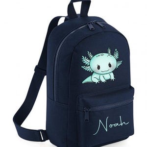 May include: A navy blue backpack with a cartoon axolotl design in light blue and white. It has a front pocket, adjustable straps, and the name "Noah" in a script font.
