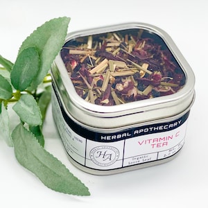 May include: A silver tin with a clear lid filled with loose leaf tea. The label reads "Herbal Apothecary Vitamin C Tea Organic Loose Leaf 2.0 oz."