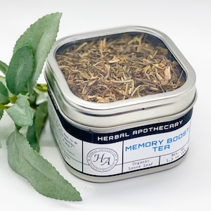 May include: A silver tin with a clear lid filled with dried herbs. The label reads "HERBAL APOTHECARY MEMORY BOOST TEA Organic Loose Leaf Net Wt. 1.3 oz."