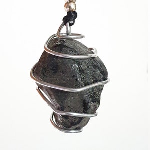 Może przedstawiać: Czarny kamienny wisiorek owinięty srebrnym drutem, wiszący na czarnym sznurku z srebrnymi koralikami.