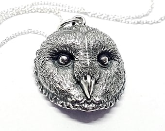 May include: A detailed silver owl pendant on a delicate chain. The pendant features a textured surface with intricate detailing of the owl's face, including large, round eyes and a sharp beak. The chain is a fine, silver link, and the background is white.