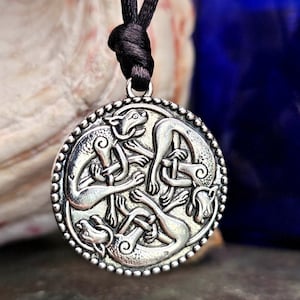 May include: Silver pendant necklace with a circular design featuring three intertwined wolves. The pendant is on a black cord.