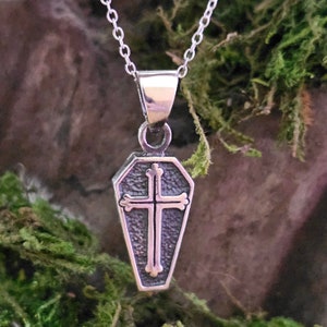 Peut inclure: Collier avec pendentif en argent représentant un cercueil avec une croix à l'intérieur. Le pendentif est suspendu à une chaîne en argent.