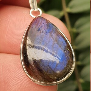 May include: A silver pendant with a teardrop-shaped labradorite gemstone. The gemstone has a dark gray base with iridescent blue and purple flashes.