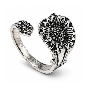 May include: A silver ring with a sunflower design. The ring has an open design, with the flower's petals and centre clearly visible. The metal has an antique finish, highlighting the floral details. The ring wraps around the finger.
