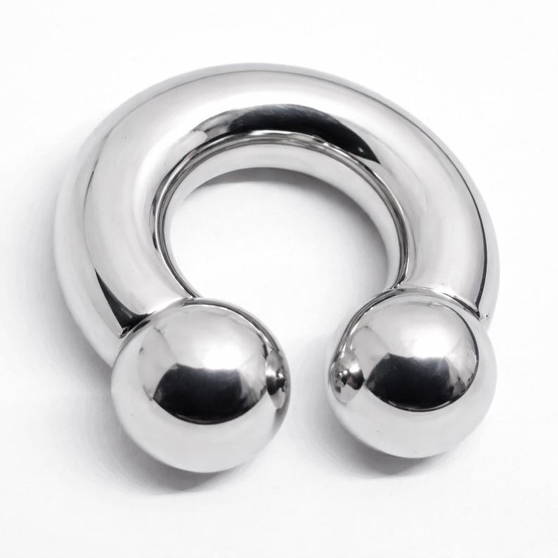 May include: A polished, silver-colored horseshoe-shaped body jewelry piece. The ends of the curved bar terminate in two spherical balls. The jewelry is designed with a smooth, reflective surface.