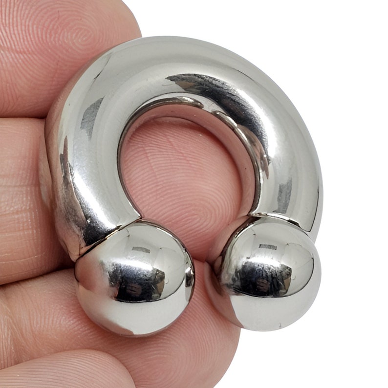 May include: A shiny, silver-colored horseshoe-shaped body jewelry piece. The ends of the horseshoe are capped with round, polished balls. The jewelry is made of a smooth, reflective metal.