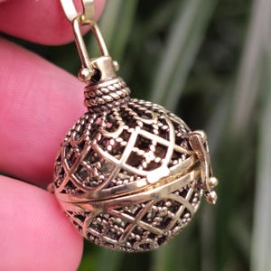 May include: A gold-toned metal cage pendant with a delicate, intricate design. The cage is open on one side and has a small loop at the top for attaching to a chain.
