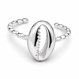 Könnte beinhalten: Ein silberfarbener Ring mit einem zentralen Kauri-Muschel-Motiv. Die Ringschiene hat eine texturierte, perlenartige Optik und ein offenes Design, das eine Anpassung ermöglicht. Die metallische Oberfläche ist poliert und reflektierend.
