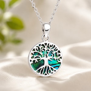 May include: A silver-toned circular pendant featuring an intricate tree of life cutout design layered over a vibrant, iridescent abalone shell inlay. The pendant hangs from a matching silver-toned link chain, showcasing a polished metallic finish.