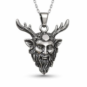 Puede incluir: Un collar con colgante plateado que presenta una detallada representación de una cara barbuda y con cuernos. El colgante tiene un acabado texturizado y cuelga de una delicada cadena. La cara tiene ojos detallados, una larga barba y astas prominentes.