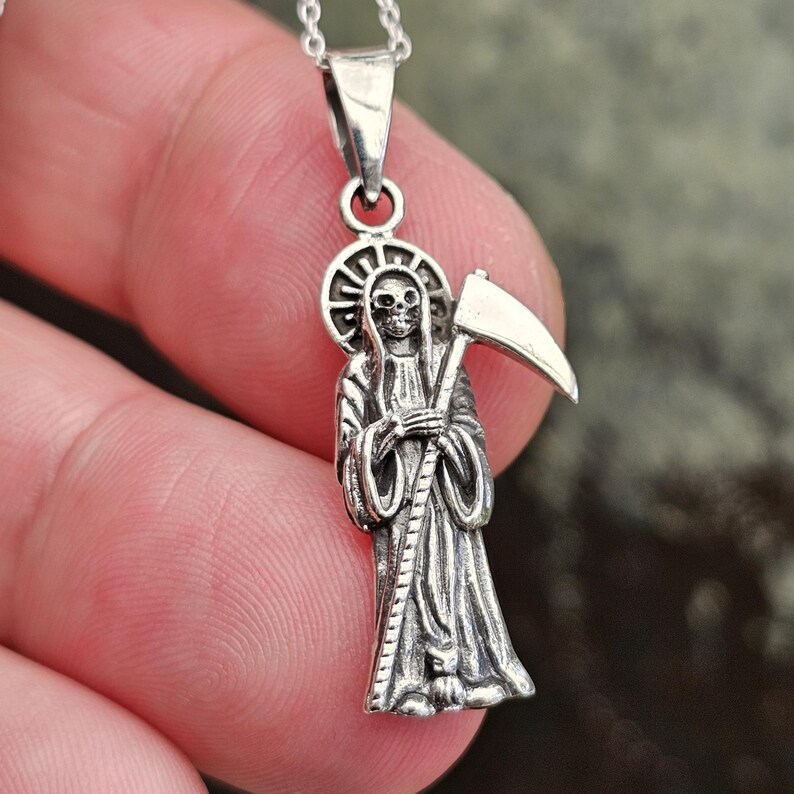 Pu&ograve; includere: Collana con ciondolo in argento che rappresenta una rappresentazione dettagliata della Morte che tiene una falce. Il ciondolo &egrave; su una catena d'argento.