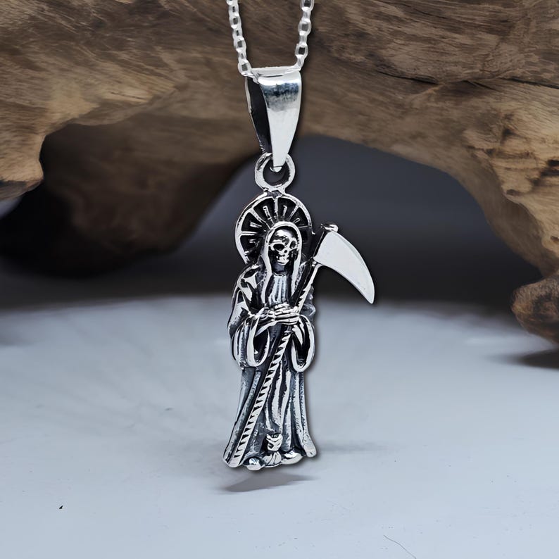 Pu&ograve; includere: Collana con ciondolo in argento che presenta una rappresentazione dettagliata della Morte che tiene una falce. Il ciondolo &egrave; su una catena d'argento.