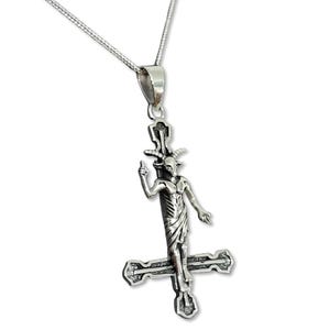 Op de afbeelding: Een zilveren ketting met een hanger met een afbeelding van een geitenkopfiguur op een omgekeerd kruis. De figuur heeft hoorns, een baard en houdt zijn hand omhoog in een gebaar van uitdaging.
